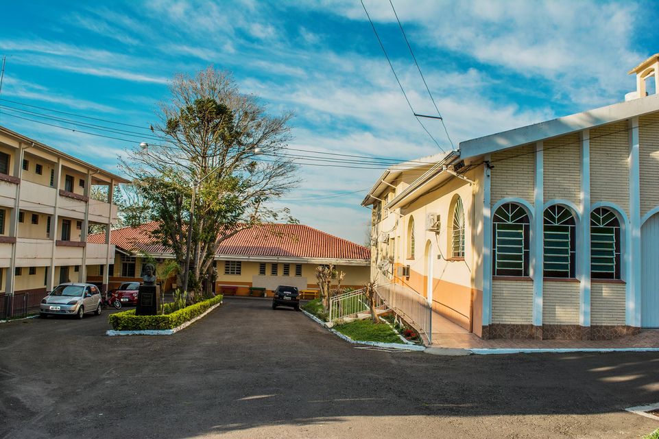 Imagem externa do lar vila itagiba durante um dia ensolarado, é amarelo com branco e há árvores e carros estacionados